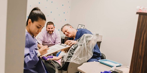 Dentist and team member treating young patient with smiling parent in room
